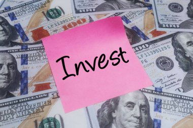 Finansal planlama, zenginlik oluşturma ve gelecekteki ekonomik büyüme stratejilerini sembolize eden 100 dolarlık banknotların üzerine el yazısıyla yazılmış pembe bir not.