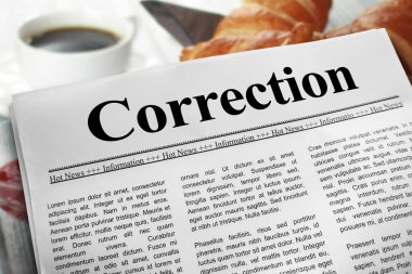 Correction newspaper layout on a breakfast table with a blurry cup of coffee and croissants in the background.