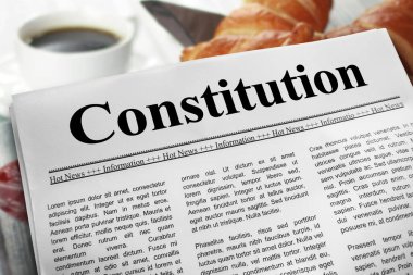 Kahvaltı masasının üzerinde gazete düzeni anayasası. Arka planda bulanık bir fincan kahve ve kruvasan var..