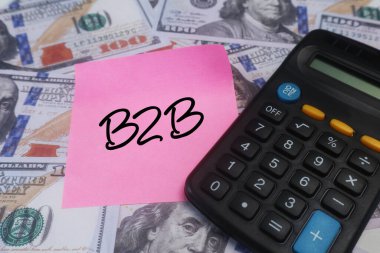 Üzerinde B2B metin, hesap makinesi ve Amerikan doları banknotları olan pembe yapışkan bir not. Ticari ticaretin iş anlayışı.
