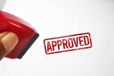 Beyaz arka planda kırmızı onaylı mürekkep mührü olan kırmızı bir kauçuk damga tutuyor. Doğrulama, izin ve başarılı doğrulamayı temsil eder.