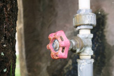 Yıpranmış pembe metal bir su vanasının dış taraftaki bir borunun gövdesine yakın çekim..