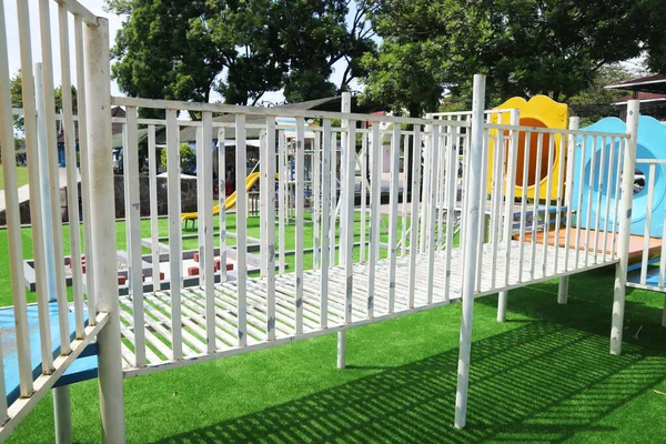 Yeşil yapay çim ve güneş gölgeleri olan bir çocuk oyun parkında beyaz metal köprü yapısı..