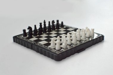 Taşınabilir satranç takımı kareli bir tahtada, birkaç gelişmiş piyon eşleşmesi için düzenlenmiş parçalar, temiz bir ışık arka planında fotoğraflanmış..