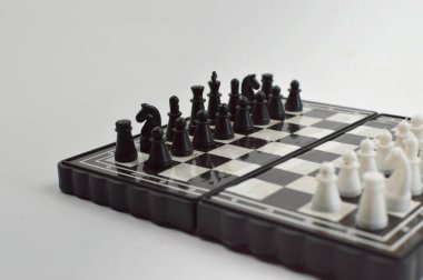 Taşınabilir satranç takımı kareli bir tahtada, birkaç gelişmiş piyon eşleşmesi için düzenlenmiş parçalar, temiz bir ışık arka planında fotoğraflanmış..