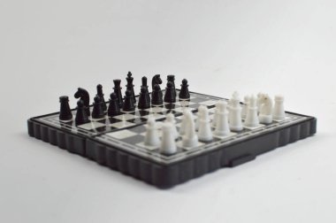 Taşınabilir satranç takımı kareli bir tahtada, birkaç gelişmiş piyon eşleşmesi için düzenlenmiş parçalar, temiz bir ışık arka planında fotoğraflanmış..