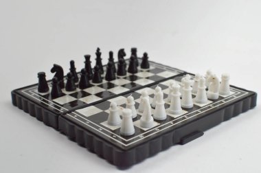 Taşınabilir satranç takımı kareli bir tahtada, birkaç gelişmiş piyon eşleşmesi için düzenlenmiş parçalar, temiz bir ışık arka planında fotoğraflanmış..