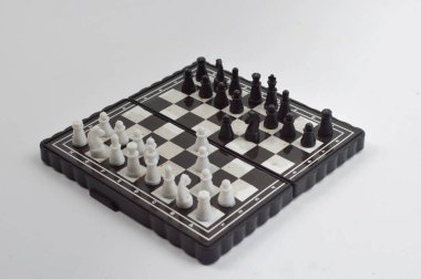 Taşınabilir satranç takımı kareli bir tahtada, birkaç gelişmiş piyon eşleşmesi için düzenlenmiş parçalar, temiz bir ışık arka planında fotoğraflanmış..