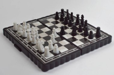 Taşınabilir satranç takımı kareli bir tahtada, birkaç gelişmiş piyon eşleşmesi için düzenlenmiş parçalar, temiz bir ışık arka planında fotoğraflanmış..