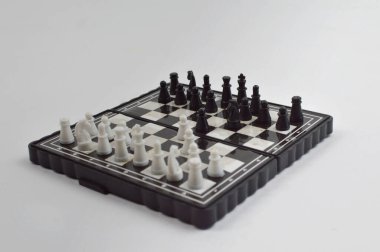 Taşınabilir satranç takımı kareli bir tahtada, birkaç gelişmiş piyon eşleşmesi için düzenlenmiş parçalar, temiz bir ışık arka planında fotoğraflanmış..