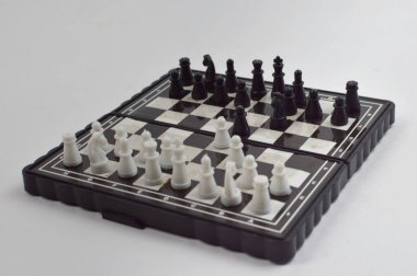 Taşınabilir satranç takımı kareli bir tahtada, birkaç gelişmiş piyon eşleşmesi için düzenlenmiş parçalar, temiz bir ışık arka planında fotoğraflanmış..