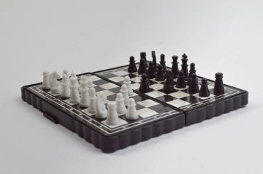 Taşınabilir satranç takımı kareli bir tahtada, birkaç gelişmiş piyon eşleşmesi için düzenlenmiş parçalar, temiz bir ışık arka planında fotoğraflanmış..