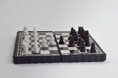 Taşınabilir satranç takımı kareli bir tahtada, birkaç gelişmiş piyon eşleşmesi için düzenlenmiş parçalar, temiz bir ışık arka planında fotoğraflanmış..