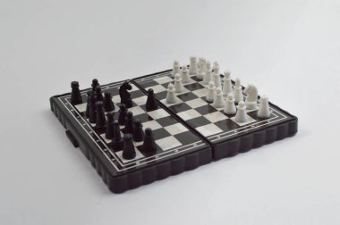 Taşınabilir satranç takımı kareli bir tahtada, birkaç gelişmiş piyon eşleşmesi için düzenlenmiş parçalar, temiz bir ışık arka planında fotoğraflanmış..