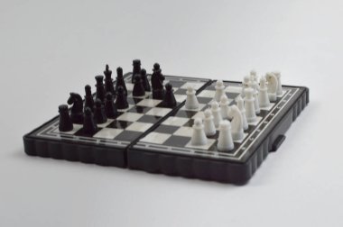 Taşınabilir satranç takımı kareli bir tahtada, birkaç gelişmiş piyon eşleşmesi için düzenlenmiş parçalar, temiz bir ışık arka planında fotoğraflanmış..