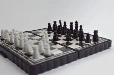 Taşınabilir satranç takımı kareli bir tahtada, birkaç gelişmiş piyon eşleşmesi için düzenlenmiş parçalar, temiz bir ışık arka planında fotoğraflanmış..