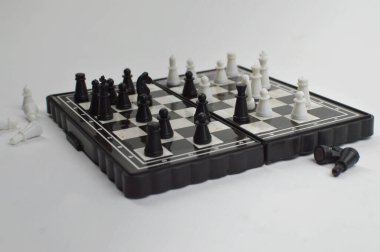 Katlanan satranç takımı masanın üzerinde duruyor ve diğerleri etrafa saçılmış durumda. Kesintili bir maç öneriliyor..