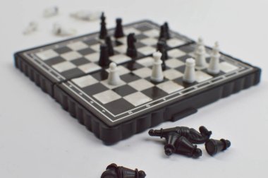 Katlanan satranç takımı masanın üzerinde duruyor ve diğerleri etrafa saçılmış durumda. Kesintili bir maç öneriliyor..