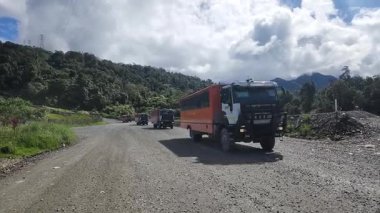 Engebeli arazi üzerinde güvenlik araçları eşliğinde bir işçi servis otobüsü, sanayi ve madencilik şirketlerinin sağladığı ulaşım hizmetlerini ön plana çıkarıyor. Papua, 10 Eylül 2025