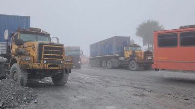 Konteynır kamyonları Papua 'daki uzak çakıl yolu boyunca 12 Kasım 2025' te sürekli hareket ederek zorlu dağlık araziden önemli kargolar taşımaktadır. Olay yeri, hayati ulaşım çabalarını yansıtıyor.