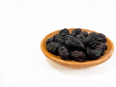 Siyah hurmalar beyaz arka planda izole edilmiş ahşap bir kasede servis edilir. Doğal kurutulmuş meyve, sağlıklı atıştırmalık ve Ramazan ve Orta Doğu mutfağı için geleneksel yemek. Kopyalama alanı ile.