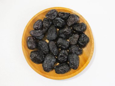 Siyah hurmalar beyaz arka planda izole edilmiş ahşap bir kasede servis edilir. Doğal kurutulmuş meyve, sağlıklı atıştırmalık ve Ramazan ve Orta Doğu mutfağı için geleneksel yemek. Üst görüntü görüntüsü.