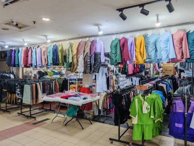 Geleneksel Malay kıyafetleri canlı bir giyim mağazasında sergileniyor, renkli Baju Melayu ve üniformaları organize bir perakende ortamında sergileniyor.