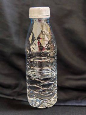 Koyu arka planda içme suyuyla dolu temiz plastik su şişesi, suyu, saflığı, tazeliği ve temiz yaşam tarzını sembolize eder.