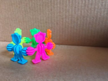 Bir dairede dizilmiş altı neon renkli oyuncak figürü, bir karton yüzey üzerinde el ele tutuşuyorlar.