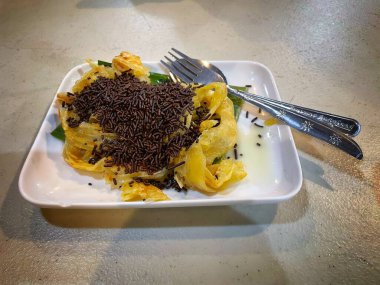 Çikolata parçacıkları ve yoğunlaştırılmış sütle lezzetli Roti Canai (ya da Paratha), çatal ve kaşıkla beyaz bir tabakta servis edilir ve tatlı ya da tatlı gibi mükemmeldir..