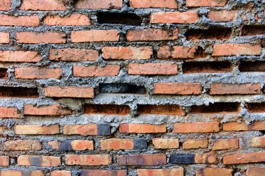 Yıpranmış, desenli, kırmızı tuğlalı bir duvar. Görünür harç ve kayıp tuğlalar. Beyaz bir boruyla çaprazlanmış..