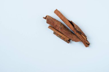 Üç tarçın çubuğundan düz bir atış. Sıcacık, topraksı tonlar ve çubukların kıvrımlı dokusu beyaz bir zeminde öne çıkıyor. Yemek, baharat, yemek ve tatil temaları için mükemmel..