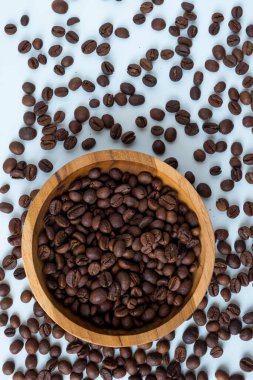 Beyaz arka planda birkaç fasulye serpiştirilmiş, robusta kahve çekirdekleri ile dolu ahşap bir kase. Kahve, kafe veya organik ürün temaları için minimalist gıda konsepti.