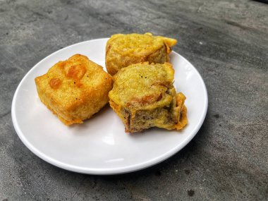 Çimento masasının üzerinde kırmızı biber sosu ve fıstık sosuyla servis edilen beyaz bir tabakta üç altın çıtır çıtır soya peyniri. Asya yemekleri, sokak yemekleri ya da mutfak temaları için mükemmel..