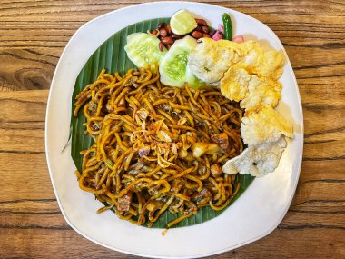 Baharatlı çorba ve sarı erişteyle dolu canlı bir tabak Endonezya Mie Aceh, yanında taze salatalık, limon, soğan turşusu ve emperyalist kraker..