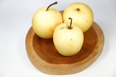Üç yuvarlak sarı armut, dörtte üçlük açıyla alınan ahşap bir tabanda servis edilir..