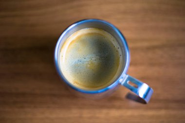 Kalın altın beyazı kremalı, paslanmaz çelikten bir bardakta, ahşap bir tahıl desenli masada servis edilen bir espresso. Kahve molası, kafein, kahve, kahve kültürü, kırsal kafe, sabah içeceği..