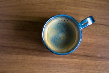 Kalın altın beyazı kremalı, paslanmaz çelikten bir bardakta, ahşap bir tahıl desenli masada servis edilen bir espresso. Kahve molası, kafein, kahve, kahve kültürü, kırsal kafe, sabah içeceği..