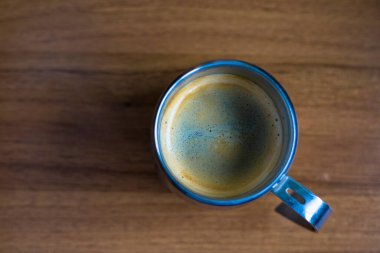 Kalın altın beyazı kremalı, paslanmaz çelikten bir bardakta, ahşap bir tahıl desenli masada servis edilen bir espresso. Kahve molası, kafein, kahve, kahve kültürü, kırsal kafe, sabah içeceği..