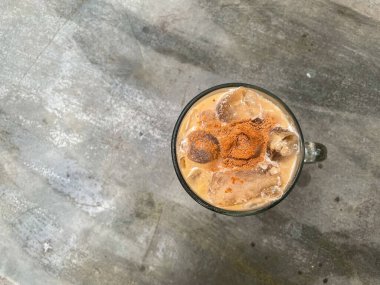 Temiz bir beton masada büyük bir bardak buzlu çikolatalı süt duruyor. Soğuk, ferahlatıcı içecek üzerine kakao tozu serpilmiş. Bu da onu menüler, içki reklamları ve yaz temaları için mükemmel kılıyor..