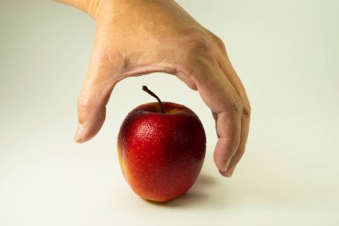 Bir el, temiz beyaz arka planda izole edilmiş canlı kırmızı ve sarı bir elmaya uzanır. Bu görüntü, sağlıklı beslenmeyi, tazeliği ve yiyeceklerin basit çekiciliğini sembolize eden seçim anını yakalar..