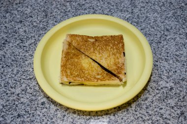 Kahverengiye kadar katlanmış ve kızartılmış bir dilim beyaz ekmek kahvaltıda siyah bir masada beyaz bir plastik tabakta servis edilir. Yukarıdan çekilmiş..