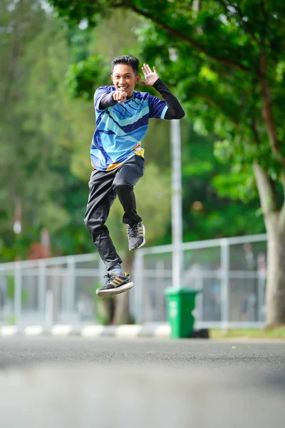 Genç enerjik bir adam neşeli bir şekilde dışarı zıplıyor, parlak bir gülümseme ve dinamik bir pozla havada yakalanıyor.