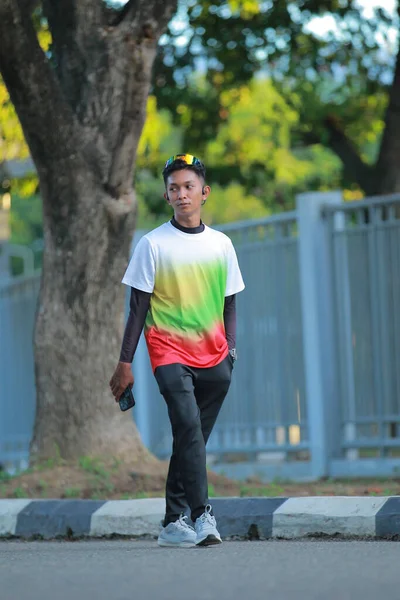 Genç bir adam rengarenk bir tişört giyerek dışarı çıkıyor.