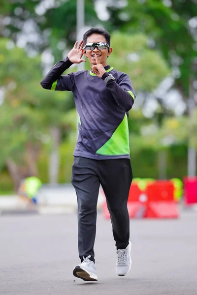 Spor kıyafetler ve güneş gözlüğü takan genç bir adam açık havada koşuyor.