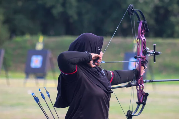 Banda Aceh, Endonezya - 7 Kasım 2025: Odaklanmış kadın okçu açık hava okçuluğu antrenmanı sırasında bir bileşik yay hedefleyen bir spor başörtüsü giyiyor