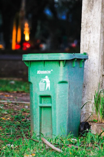 Banda Aceh, Endonezya - 18 Kasım 2025: Kamu parkında beton bir direğin yanına yerleştirilmiş yeşil bir açık hava çöp kutusu