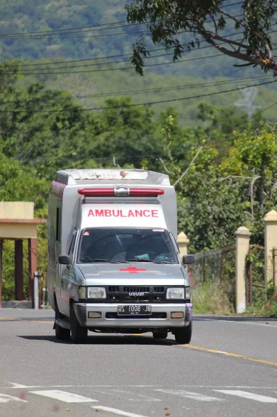 Aceh Besar, Endonezya - 11 Aralık 2025: Arka planda yemyeşil bitki örtüsü ve tepelerle çevrili kırsal bir yol boyunca giden eski bir Isuzu ambulansı
