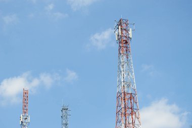 Açık mavi gökyüzüne karşı yükselen antenleri ve vericileri olan çoklu telekomünikasyon kuleleri
