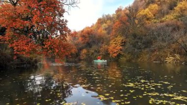 Sonbahar yaprakları sakin bir nehrin yüzeyinde süzülür. Etrafındaki ağaçları yansıtır. Balıkçılar huzurlu bir kano yolculuğunun keyfini çıkarırlar.